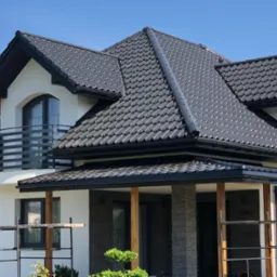 Nowoczesny dom jednorodzinny z ciemnoszarą dachówką ceramiczną, czarnymi rynnami i obróbkami blacharskimi, widoczne rusztowania na pierwszym planie.