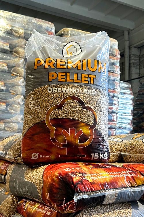 Ułożone worki z pelletem drzewnym Premium Pellet DrewNoLand 6mm 15kg, z widocznym logo w kształcie płomienia drzewa na tle magazynowym.