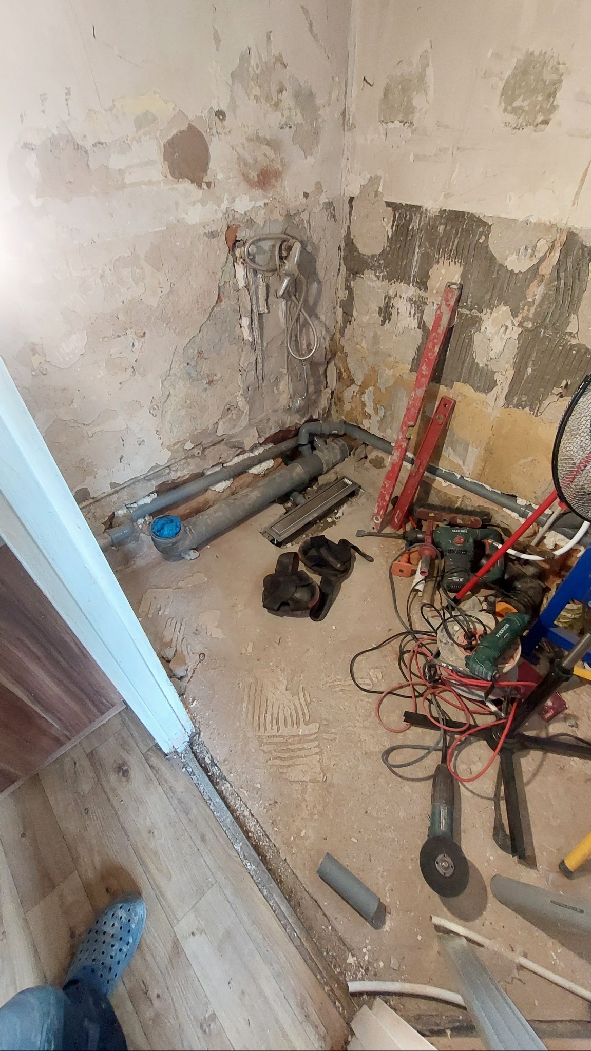Fragment łazienki w trakcie remontu: widoczne rury kanalizacyjne, narzędzia i uszkodzone ściany. Ujęcie z góry, podkreślające etap prac instalacyjnych.