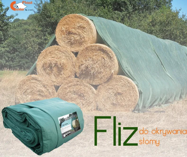 Stóg siana przykryty zieloną włókniną, w tle drzewa, na pierwszym planie zwinięta włóknina z etykietą.