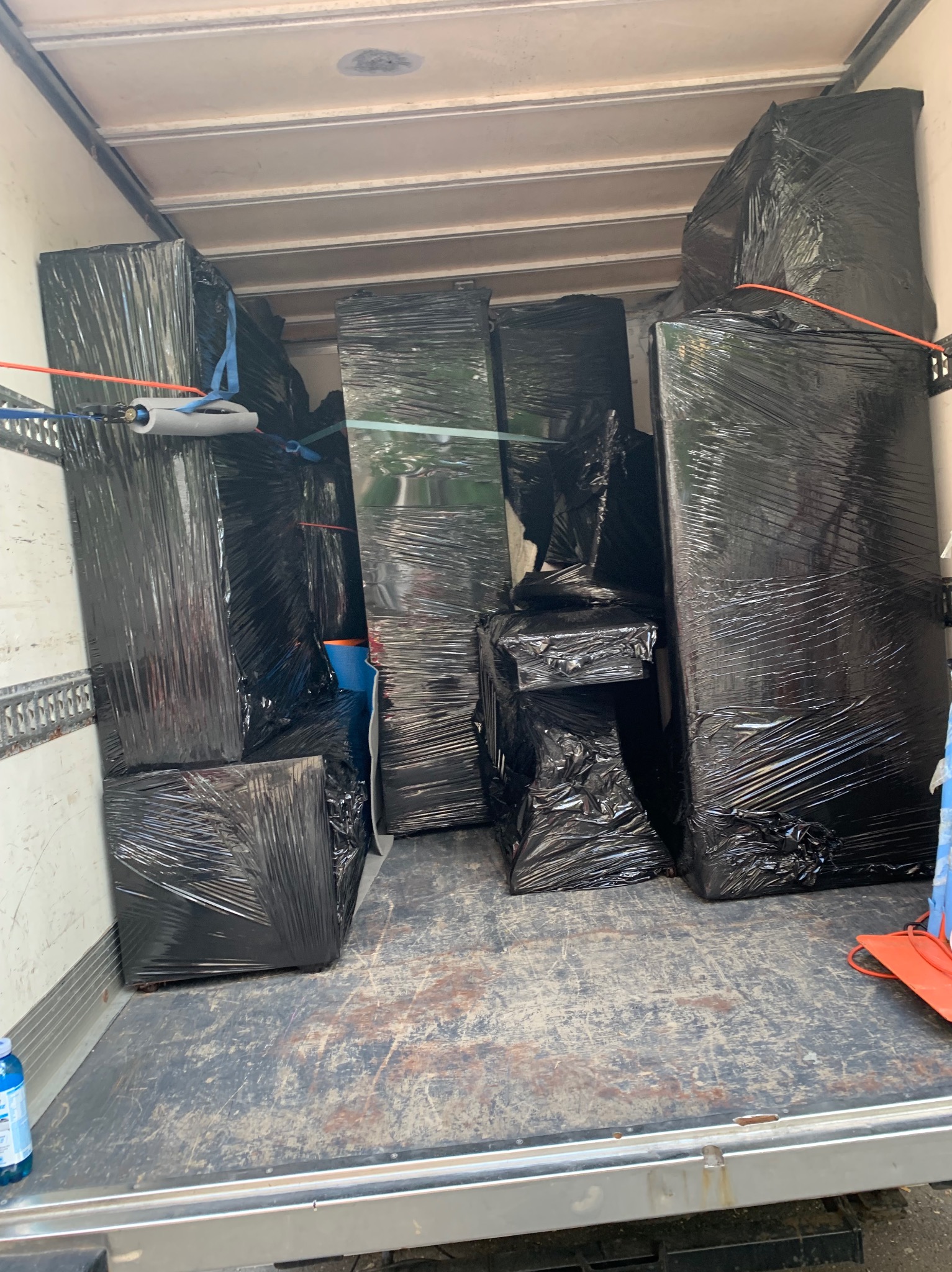 Wnętrze samochodu dostawczego wypełnione meblami owiniętymi czarną folią stretch, zabezpieczonymi pasami transportowymi.