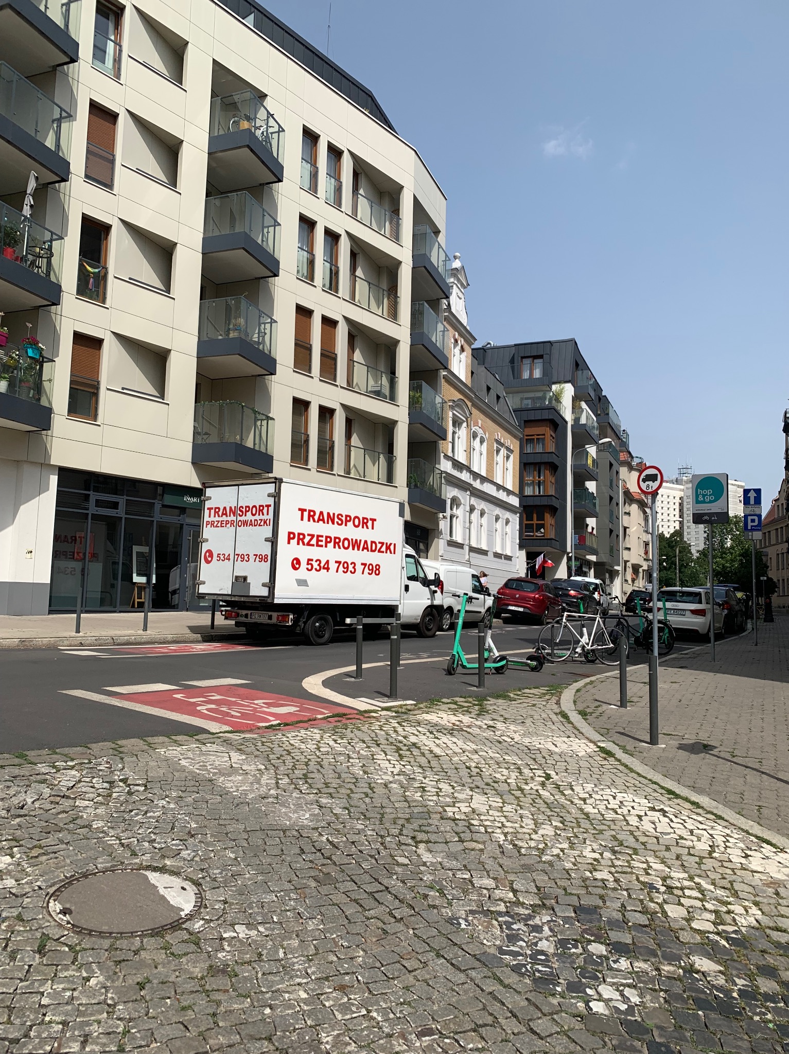 Ciężarówka z reklamą usług transportowych zaparkowana na ulicy w mieście, z widocznymi budynkami mieszkalnymi w tle.