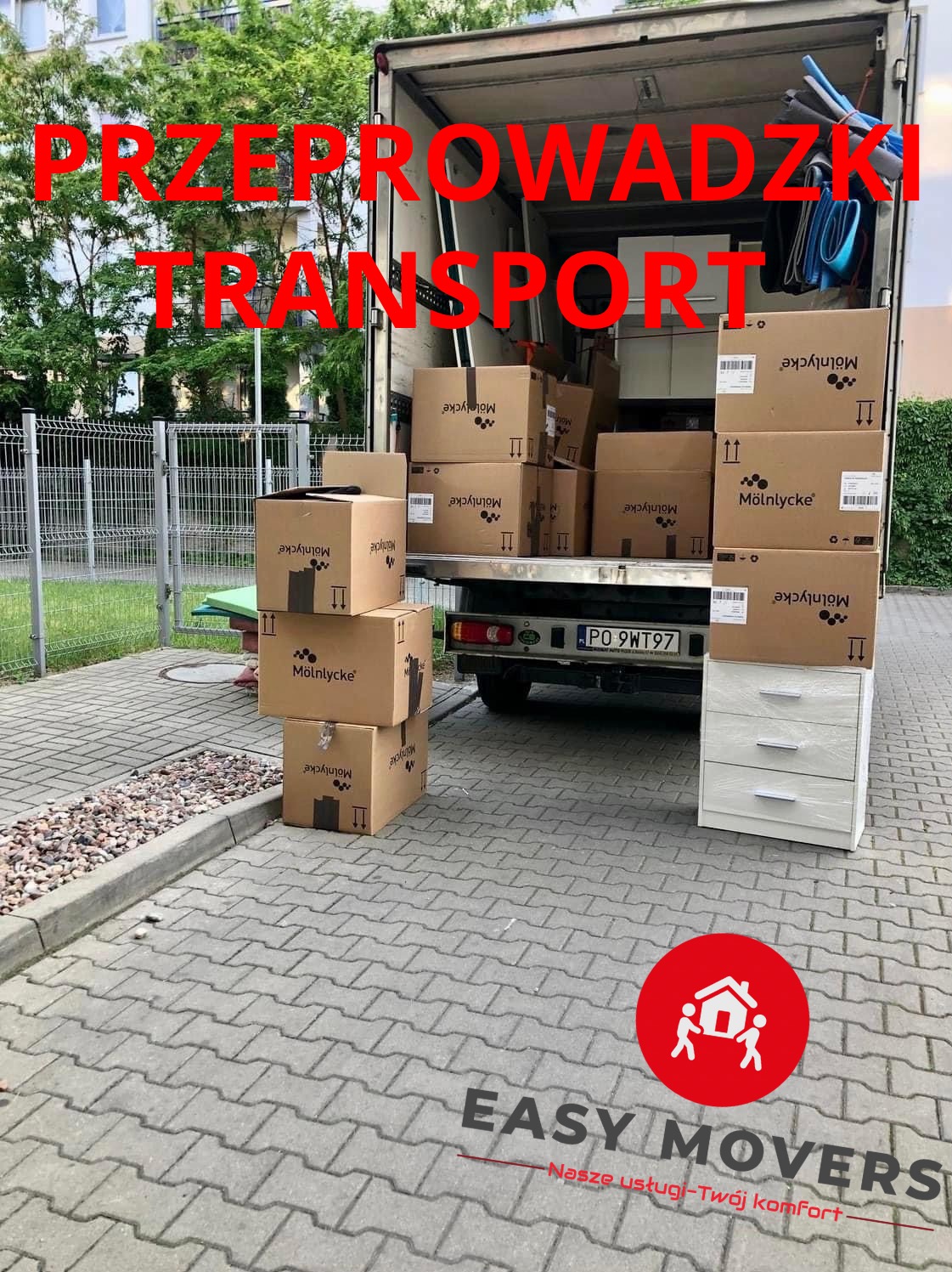 Częściowo załadowany samochód dostawczy z kartonami firmy Mölnlycke i białą komodą na chodniku przed budynkiem.