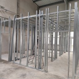 Everest - Metalowa konstrukcja szkieletowa ścian działowych w surowym stanie, widoczna drabina i instalacje pod sufitem.