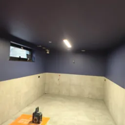 Wykończone wnętrze piwnicy z ciemnoniebieskim sufitem, jasnymi płytkami na ścianach i podłodze. Widoczne gniazdka elektryczne i narzędzie na podłodze.