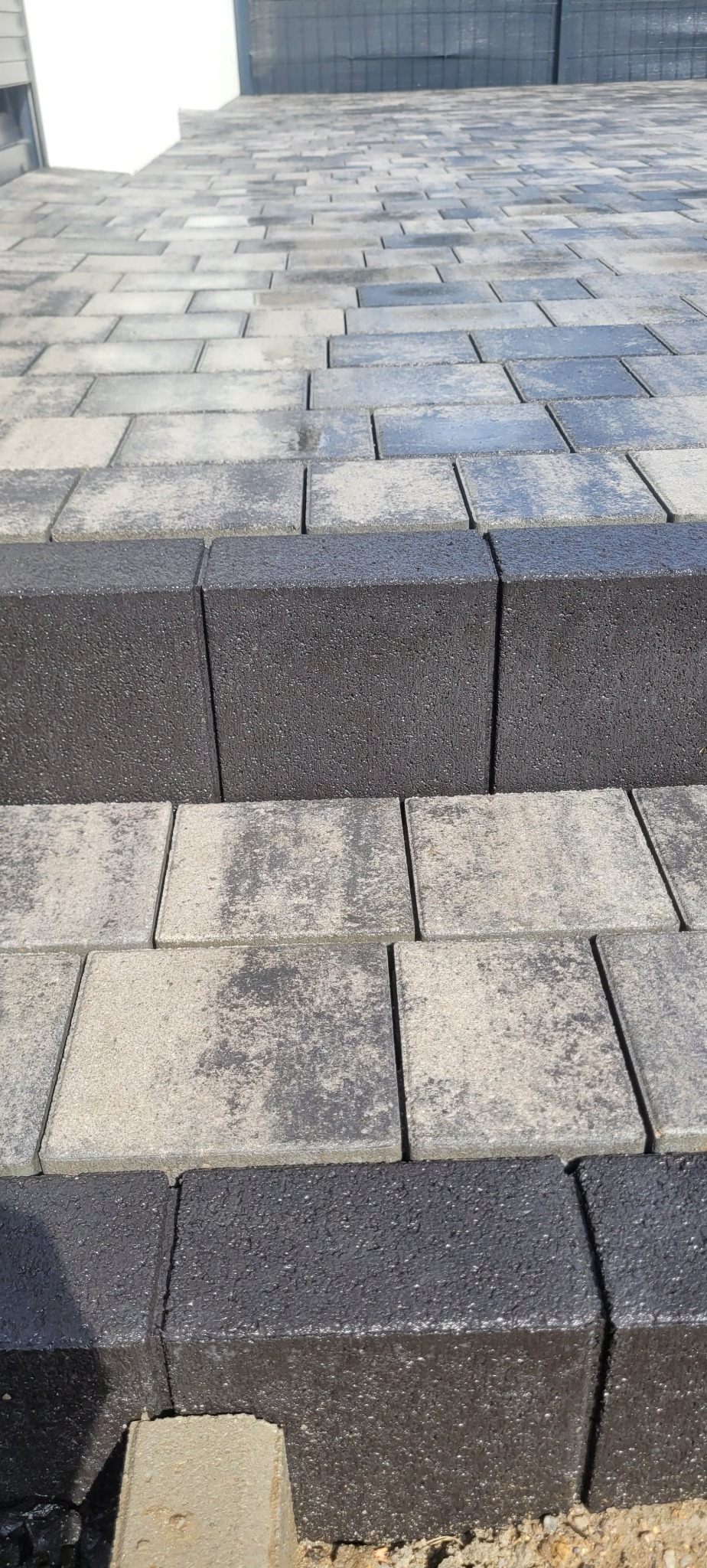 Ułożona kostka brukowa w odcieniach szarości i czerni, tworząca schody. Widoczne detale faktury kostki i precyzyjne ułożenie. Ujęcie z bliska, podkreślające jakość wykonania.