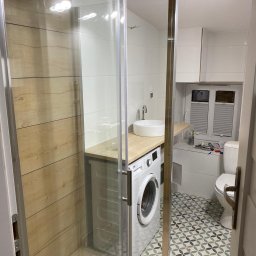 AJP INVESTED Adam Porębny - Nowoczesna łazienka z kabiną prysznicową typu walk-in, pralką pod umywalką na drewnianym blacie, białą armaturą i wzorzystą podłogą w odcieniach szarości i błękitu.