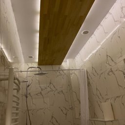 AJP INVESTED Adam Porębny - Nowoczesna łazienka z marmurowymi płytkami, drewnianym panelem na suficie z oświetleniem LED, deszczownicą i grzejnikiem drabinkowym.