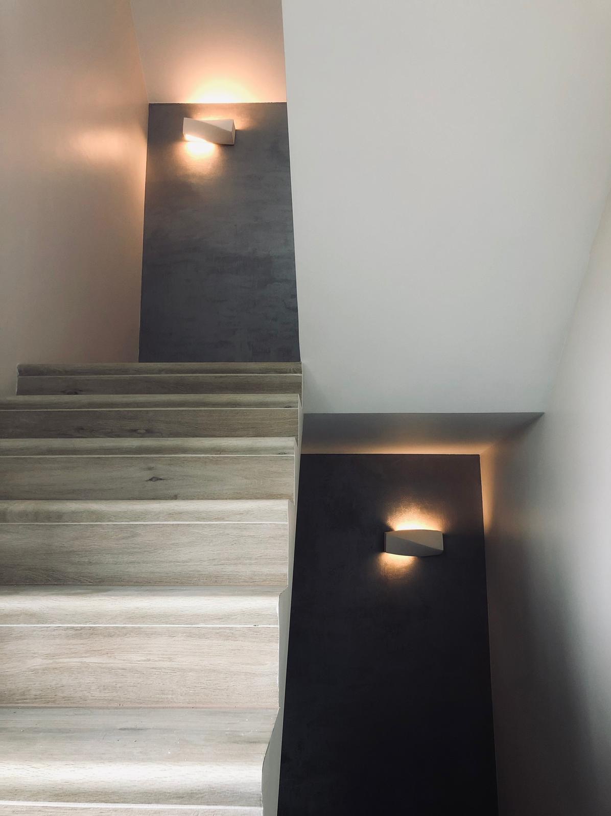 Schody wykończone panelami drewnopodobnymi, oświetlone kinkietami na ścianie w kolorze grafitowym.