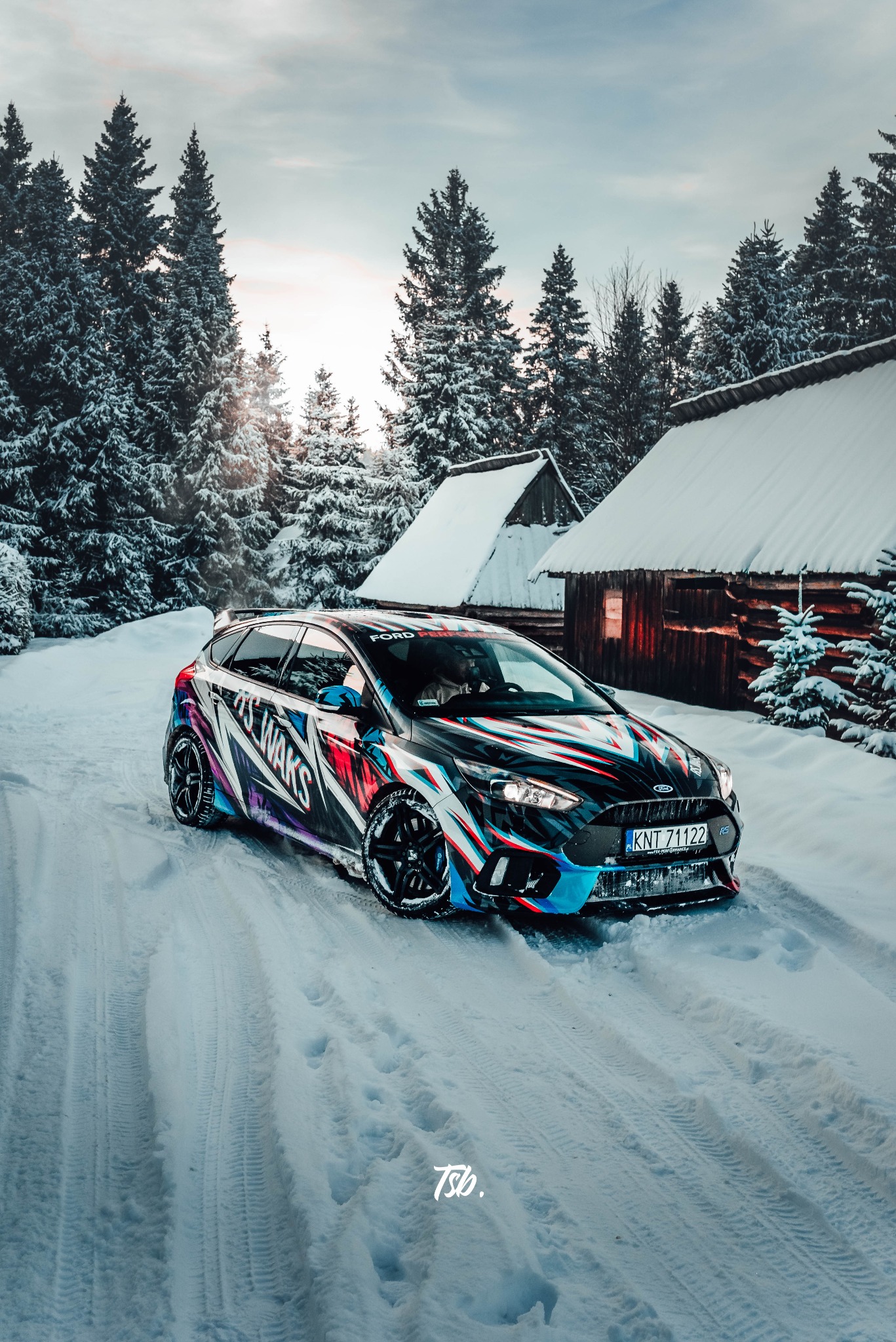 Ford Focus RS z niestandardowym, kolorowym oklejeniem karoserii na tle zasypanych śniegiem domków i drzew