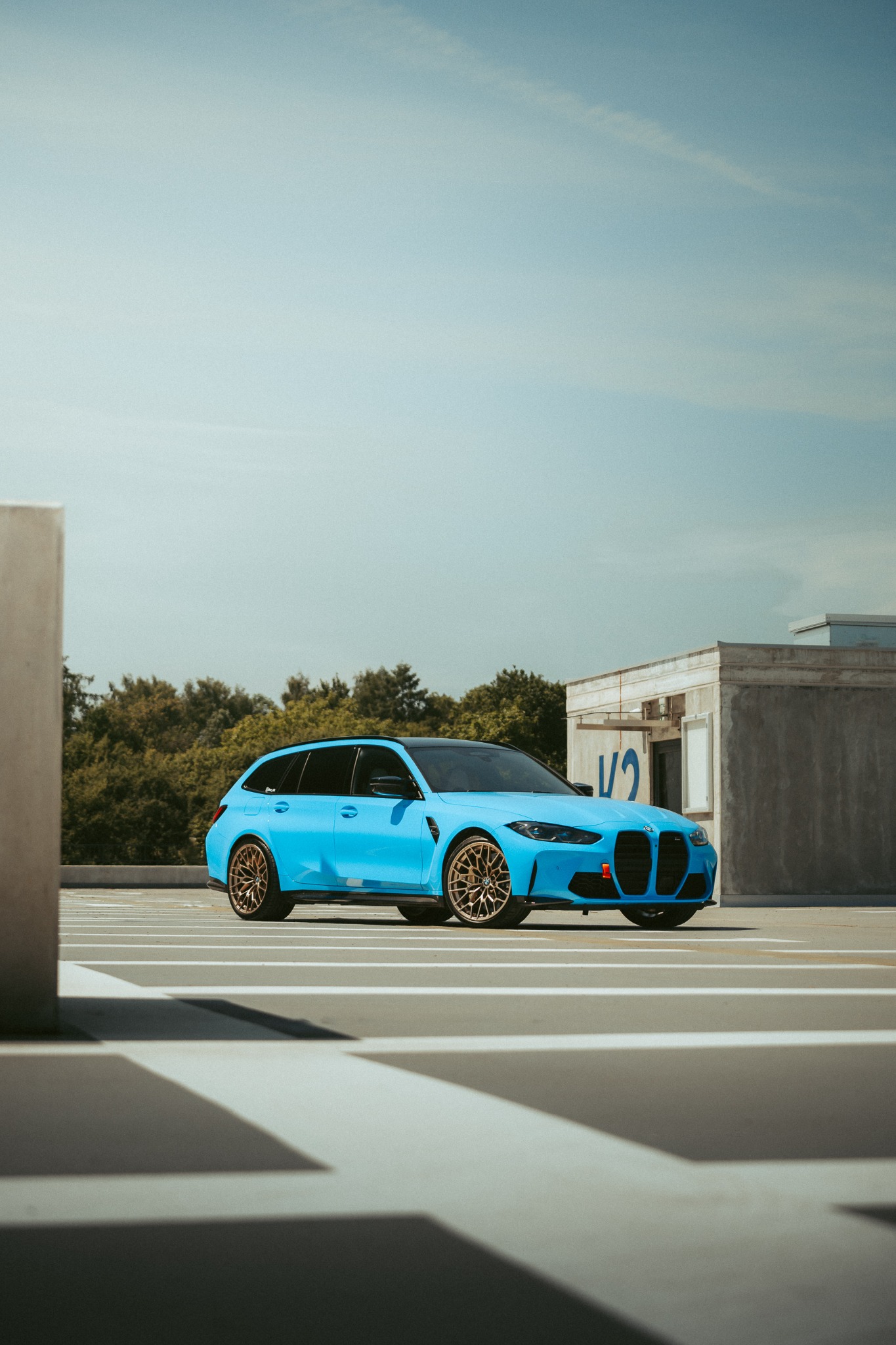 Jasnoniebieskie kombi na parkingu wielopoziomowym, z brązowymi felgami i czarnym dachem, widziane z niskiej perspektywy.