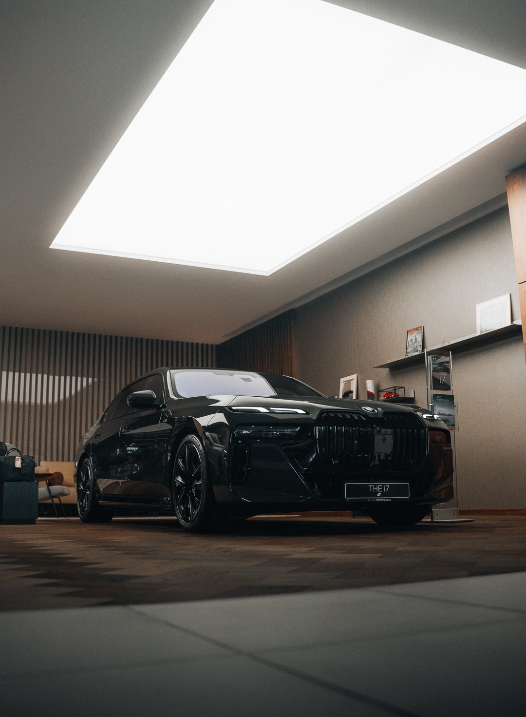 Czarny samochód BMW i7 zaparkowany w nowoczesnym salonie z oświetleniem sufitowym, widoczny z przodu, z detalami na grillu i logo.