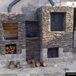 Ogródek z kamiennym grillem i piecem chlebowym, z miejscem na drewno i z kutymi drzwiczkami, wykończony drobnymi płytkami kamiennymi.