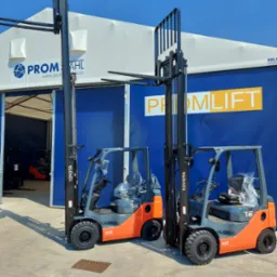 Dwa nowe wózki widłowe Toyota stojące przed halą z logo Promlift, jeden z wózków ma jeszcze folię ochronną na siedzeniu.
