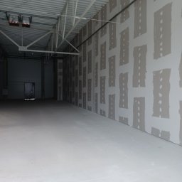 PAW-BUD USŁUGI OGÓLNOBUDOWLANE PAWEŁ KUREK - Wnętrze hali produkcyjnej z zamontowanymi płytami na ścianach, częściowo pokrytymi masą wyrównującą, widoczne szpary między płytami wypełnione masą.