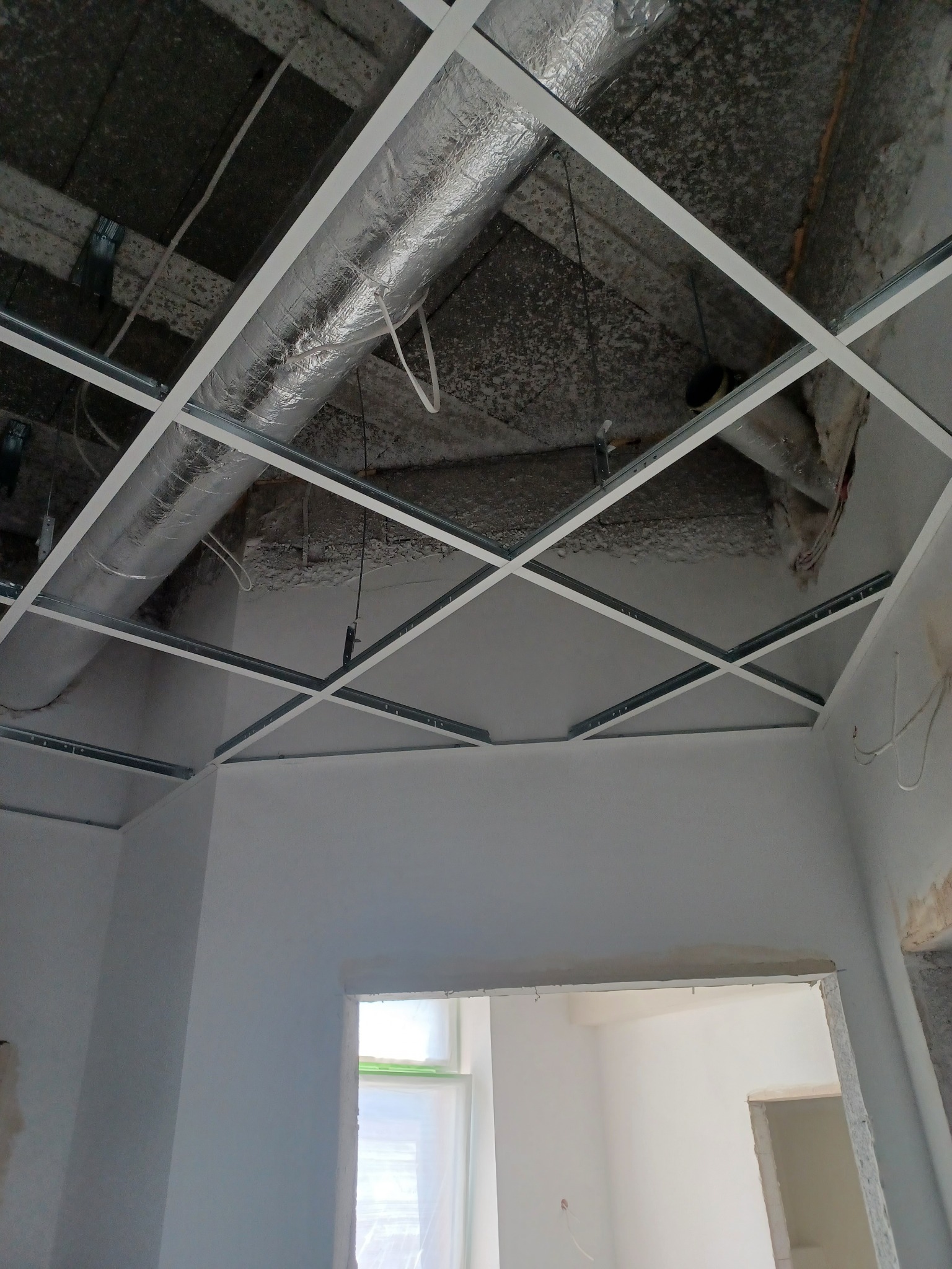 Montaż metalowej konstrukcji sufitu podwieszanego z widocznymi elementami instalacji wentylacyjnej w surowym stanie.