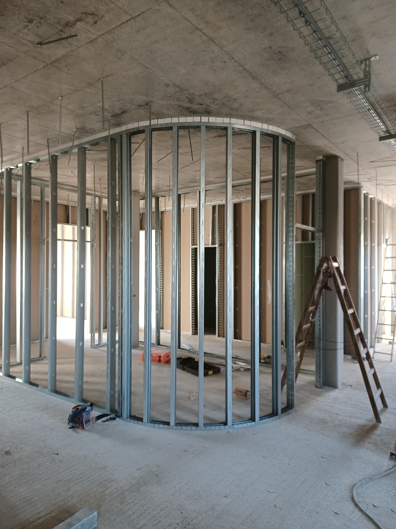 Stelaż metalowy pod zabudowę ścian działowych z elementem łukowym, widoczne narzędzia i drabina w surowym stanie deweloperskim.