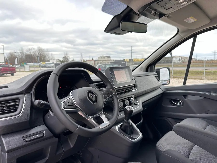 Wnętrze nowoczesnego busa Renault z manualną skrzynią biegów, widok z perspektywy pasażera na deskę rozdzielczą, kierownicę z logo Renault i ekran nawigacji.