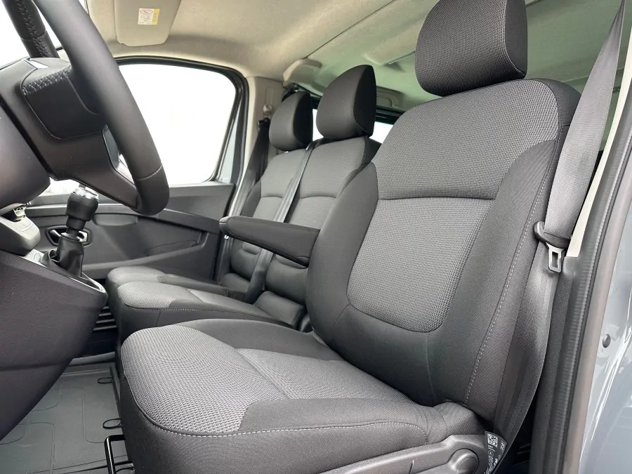 Wnętrze busa z tapicerką w odcieniach szarości, widok na przednie siedzenia z regulowanym podłokietnikiem i pasami bezpieczeństwa.