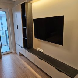 Meble JM - Michał Wyka - Nowoczesna zabudowa meblowa z szafkami i półkami w salonie, wykończona w bieli i czarnym marmurze, z telewizorem na ścianie i drewnianą podłogą.
