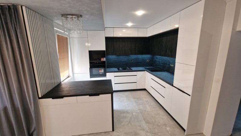 Nowoczesna kuchnia w bieli i czerni z wyspą, oświetleniem punktowym i dekoracyjną zasłoną. Minimalistyczny design z akcentami glamour.