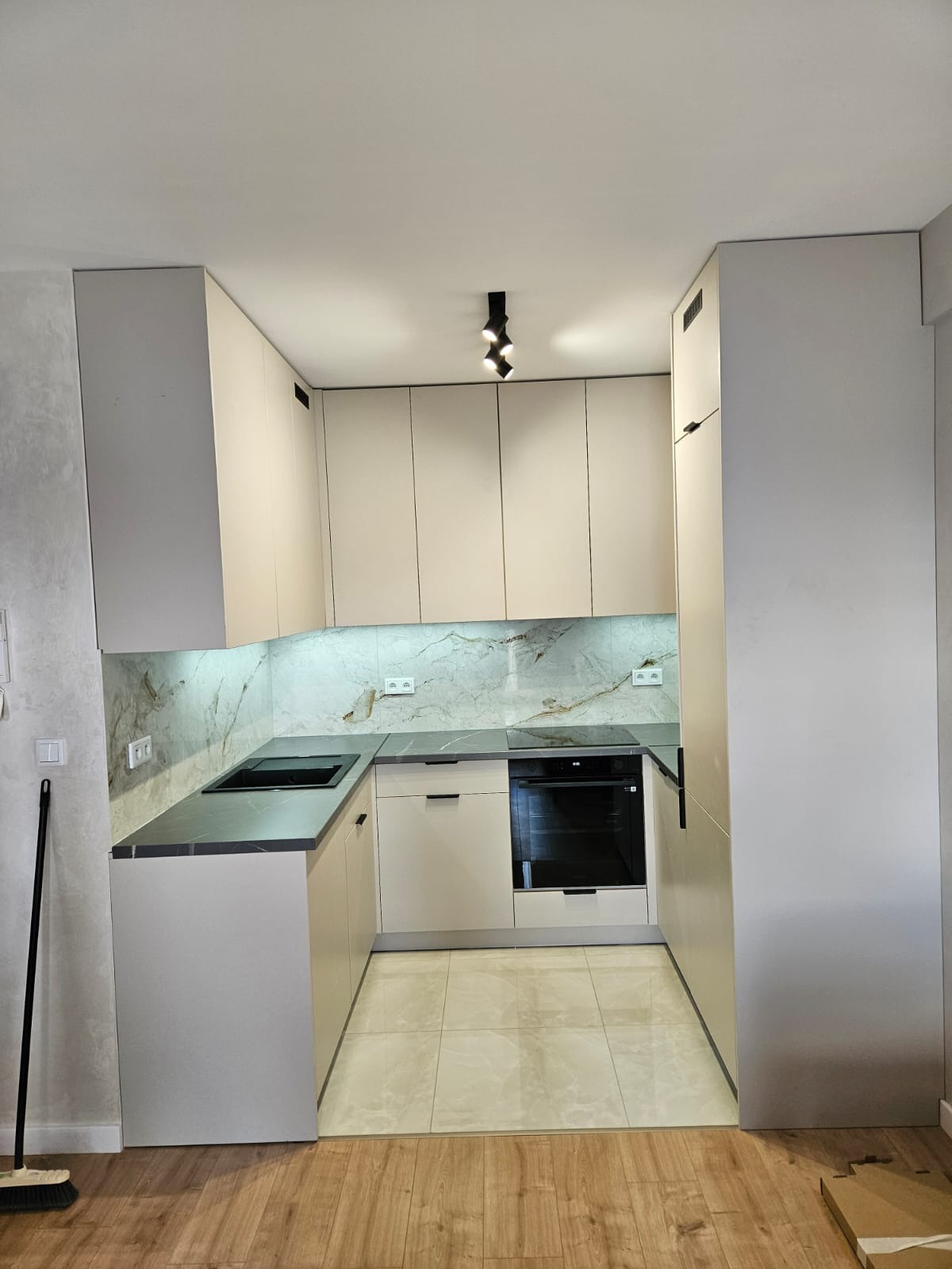 Jasna kuchnia na wymiar z marmurowym blatem i oświetleniem punktowym. Minimalistyczny design, widok na zabudowę kuchenną z płytą i zlewem.