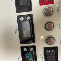 Ru-Bud - Panel sterowania z wyświetlaczami napięcia i stanu baterii, bezpieczniki i oznaczenia napięć. Widoczne kable i elementy instalacji elektrycznej.