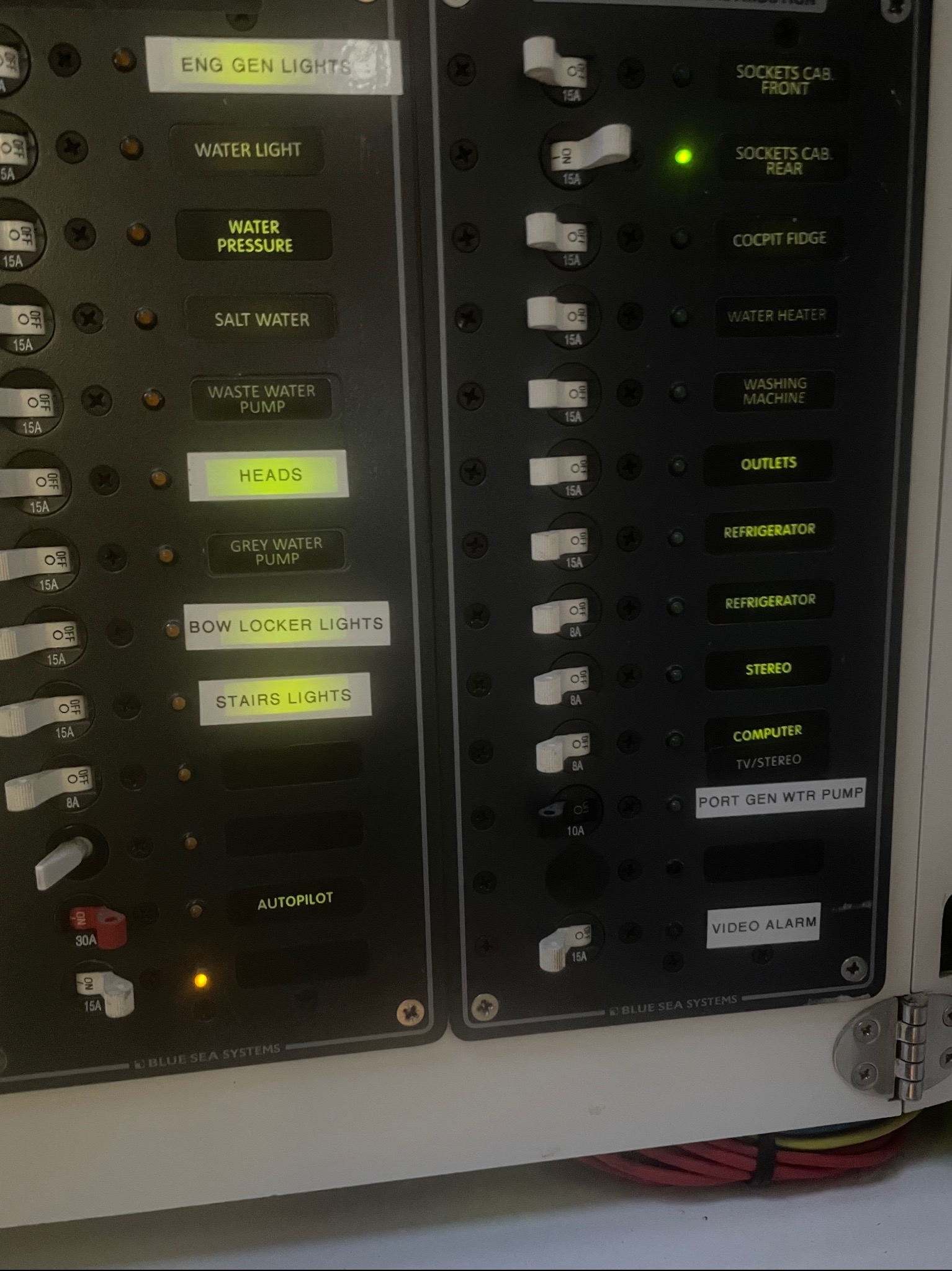 Panel sterowania Blue Sea Systems z przełącznikami i bezpiecznikami oznaczonymi dla różnych funkcji, takich jak oświetlenie, pompy i urządzenia. Widoczne diody sygnalizacyjne.