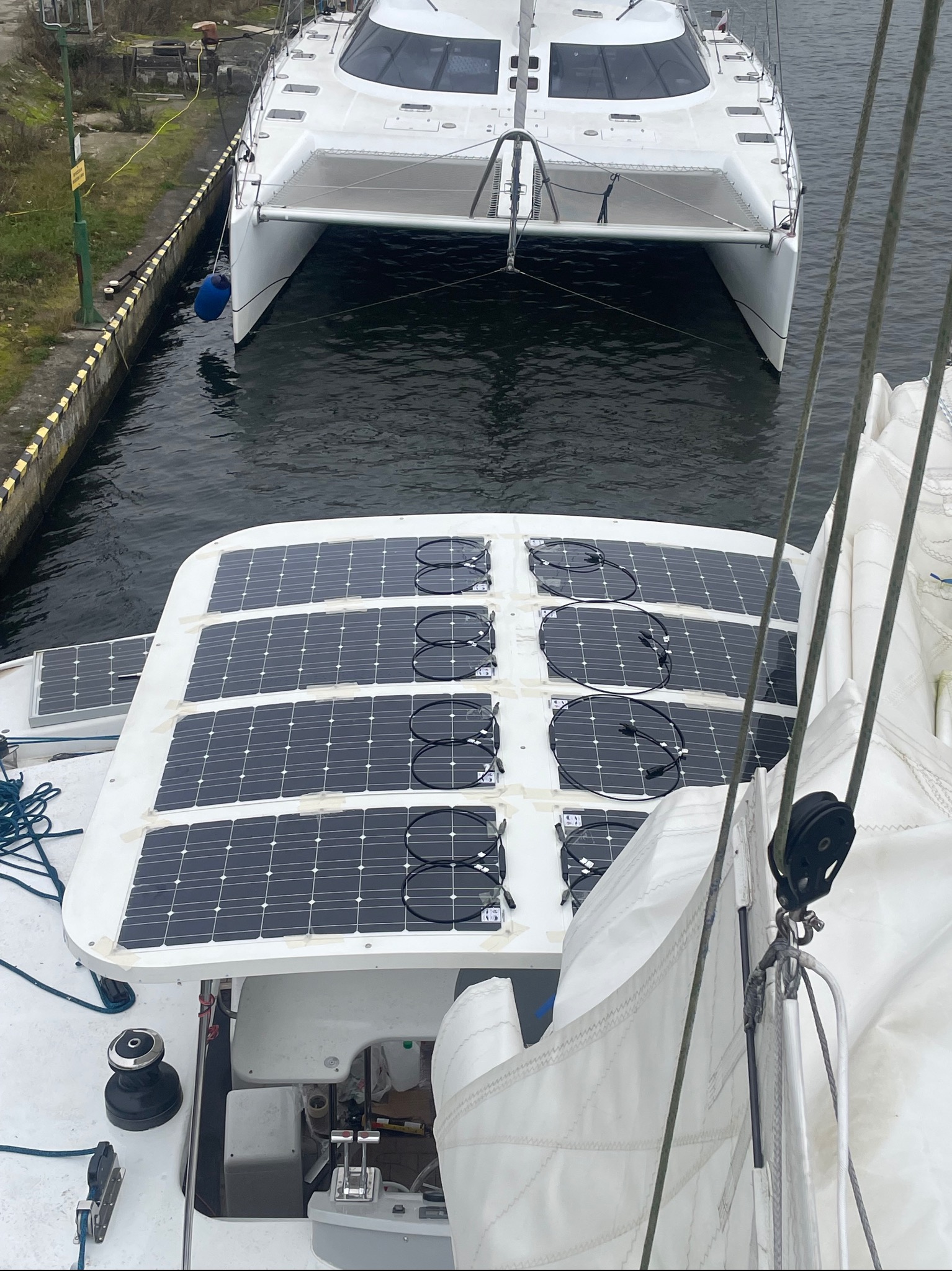 Widok z góry na jacht z panelami słonecznymi na pokładzie, zacumowany w porcie. W tle widoczny drugi jacht.