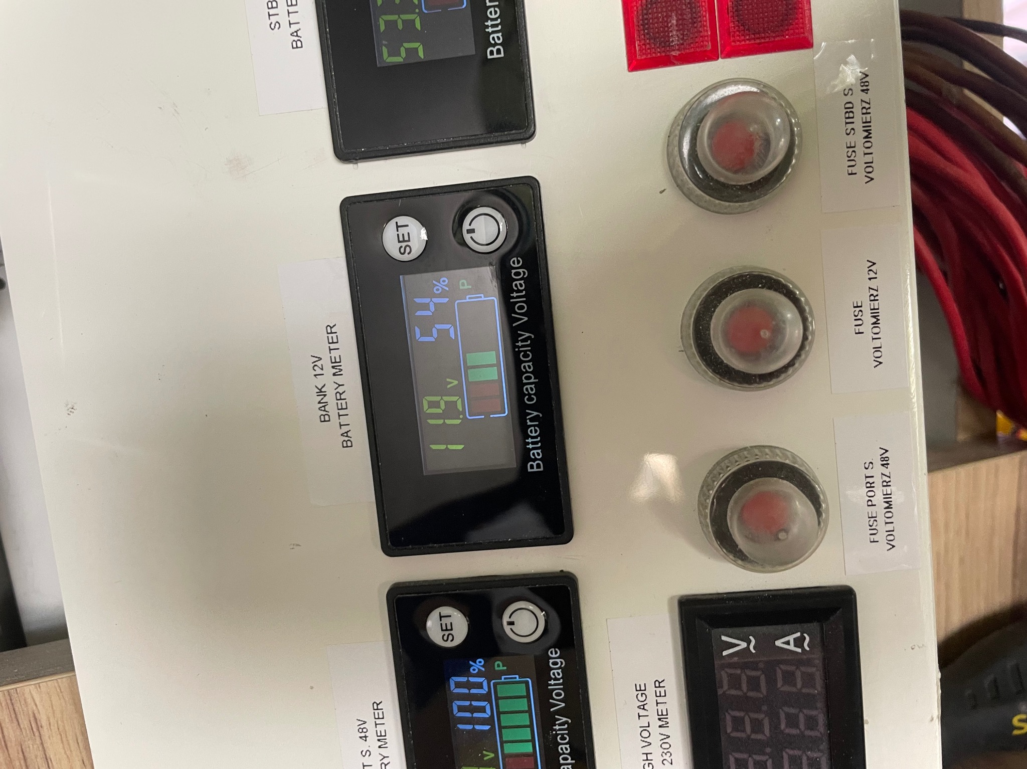 Panel sterowania z wyświetlaczami napięcia i stanu baterii, bezpieczniki i oznaczenia napięć. Widoczne kable i elementy instalacji elektrycznej.