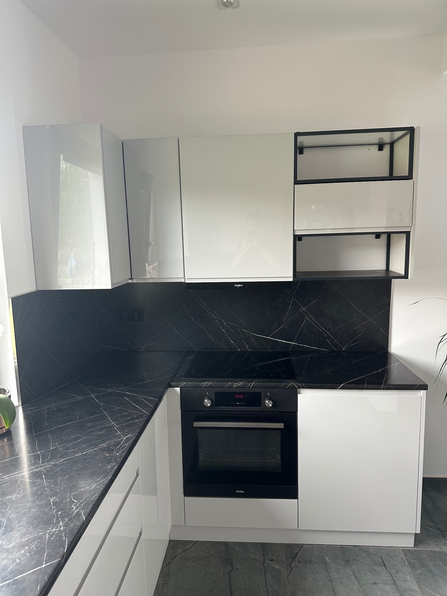 Biała, lakierowana kuchnia na wymiar we Wrocławiu z blatem i ścianą nad blatem imitującymi czarny marmur, z piekarnikiem Amica i otwartymi półkami z czarnymi ramami.