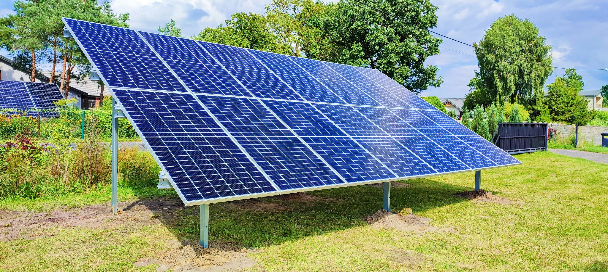 Panel słoneczny na metalowych podporach ustawiony na trawniku przed domem w słoneczny dzień.