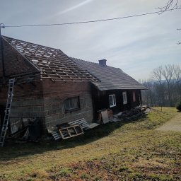 Andrzej Puchała PA&Synowie - Dom z częściowo zdjętym dachem, widoczna konstrukcja więźby dachowej, drabina oparta o ścianę, teren trawiasty.