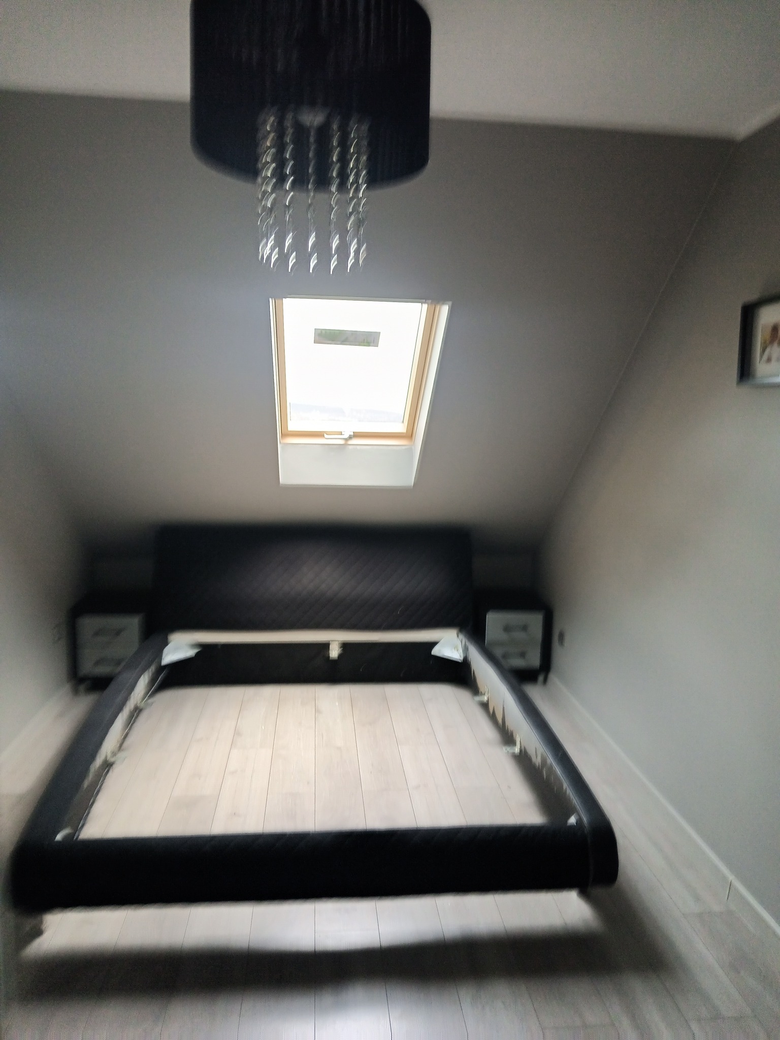 Poddasze z oknem dachowym i ramą łóżka, widok z dołu na sufit z lampą.