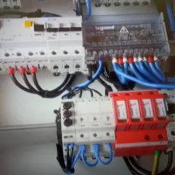 Tablica rozdzielcza z zainstalowanymi zabezpieczeniami przepięciowymi, wyłącznikami i przewodami w kolorach niebieskim i czarnym, widoczne elementy marki Legrand i Eaton.