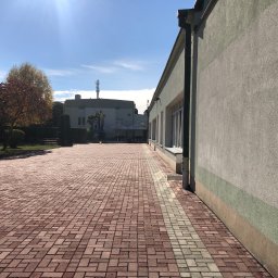 Profesjonalne czyszczenie elewacji budynków, dachów oraz kostki brukowej, Mateusz Leniar - Budynek z elewacją w odcieniach szarości i zieleni, obok czerwona kostka brukowa z szarym pasem, widok z perspektywy chodnika w słoneczny dzień.