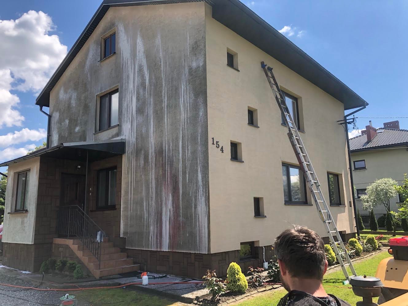 Dwukondygnacyjny dom z częściowo umytą elewacją, widoczne zacieki po czyszczeniu, drabina oparta o ścianę, numer domu 154.