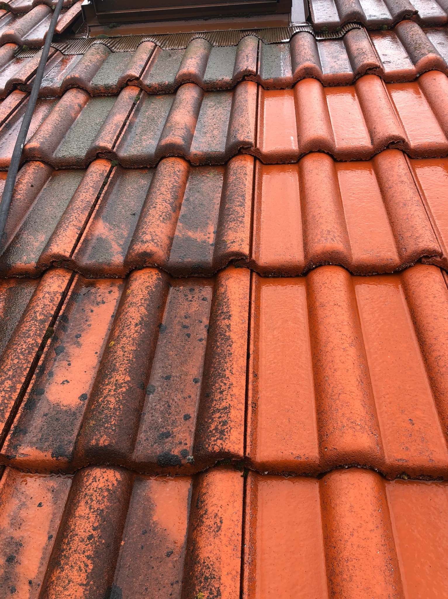 Częściowo umyty dach z czerwonej dachówki ceramicznej, widoczna różnica między czystą a zabrudzoną powierzchnią, mokra powierzchnia po myciu.
