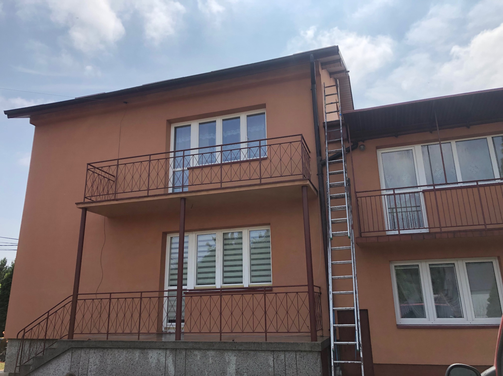 Dwupiętrowy budynek z balkonami i przystawioną aluminiową drabiną, gotowy do prac na elewacji.