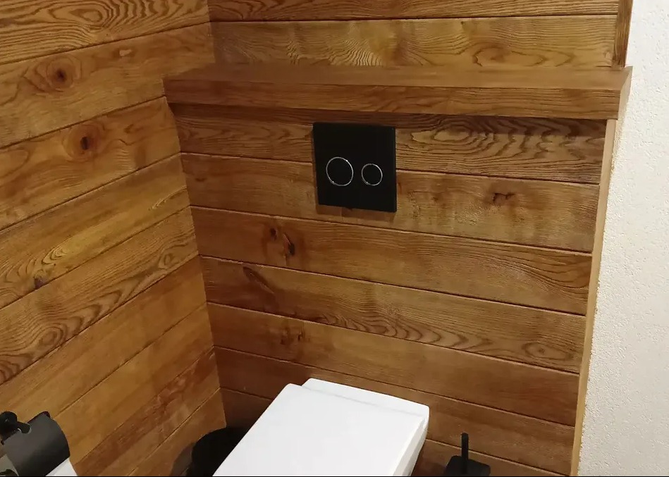 Drewniana boazeria w łazience z nowoczesnym panelem spłukującym i widocznym fragmentem toalety.