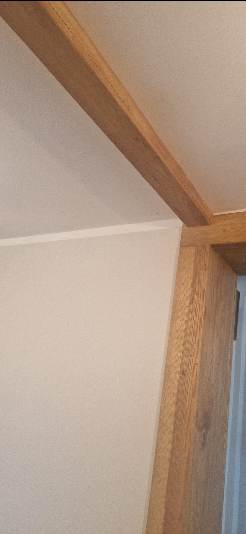 Wnętrze z drewnianą belką stropową i kolumną przy ścianie pomalowanej na biało, widok z dołu.