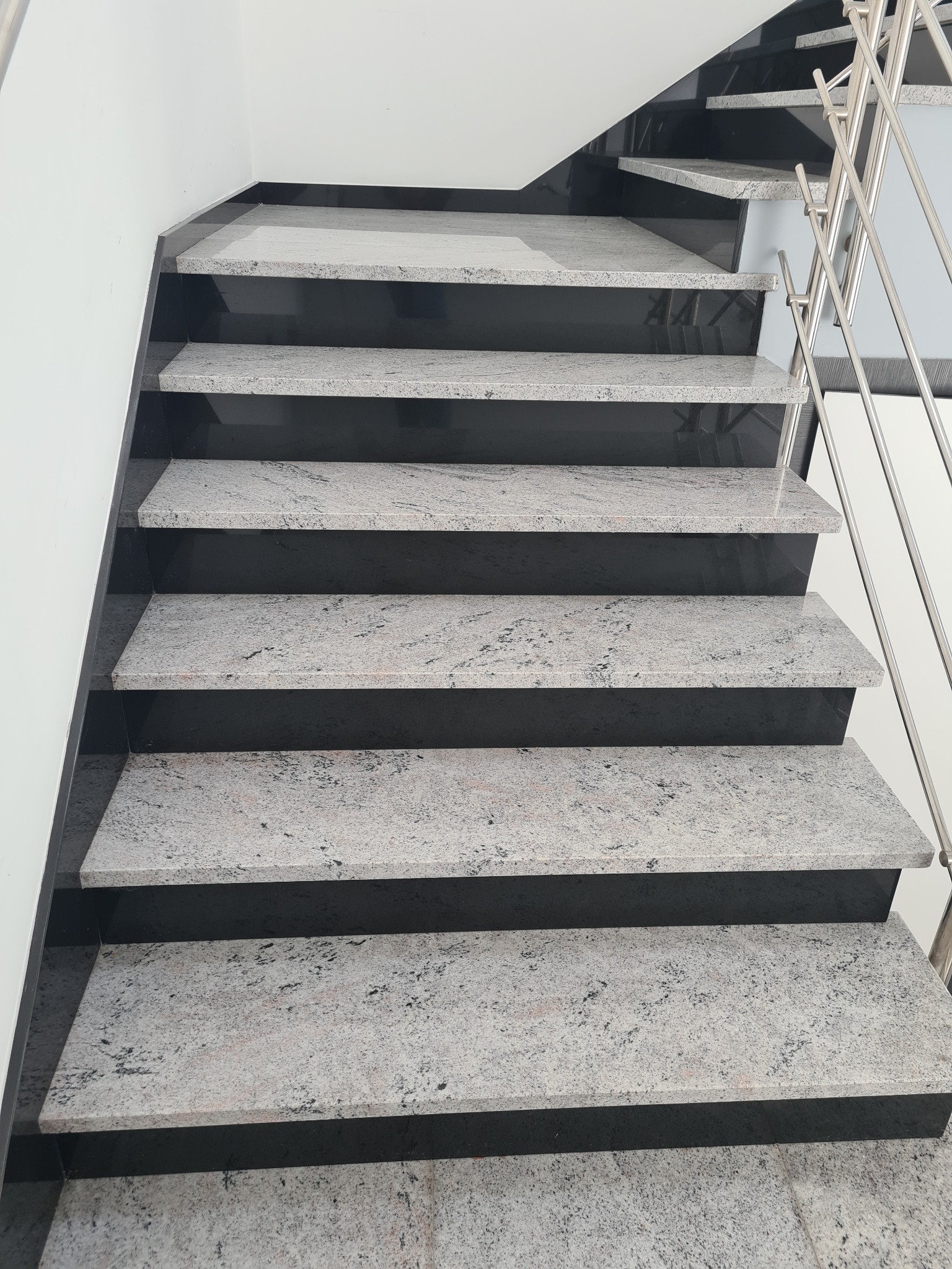 Schody wewnętrzne z szarego kamienia z ciemnymi podstopnicami i metalową balustradą, widok z dołu.