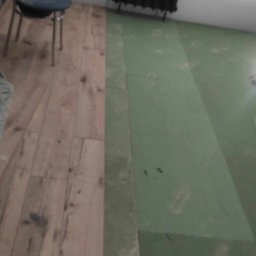 Mikołaj Skrzypczyk - Fragment podłogi w trakcie prac: część wyłożona panelami imitującymi drewno, część z zielonym podkładem, w tle grzejnik i krzesło.