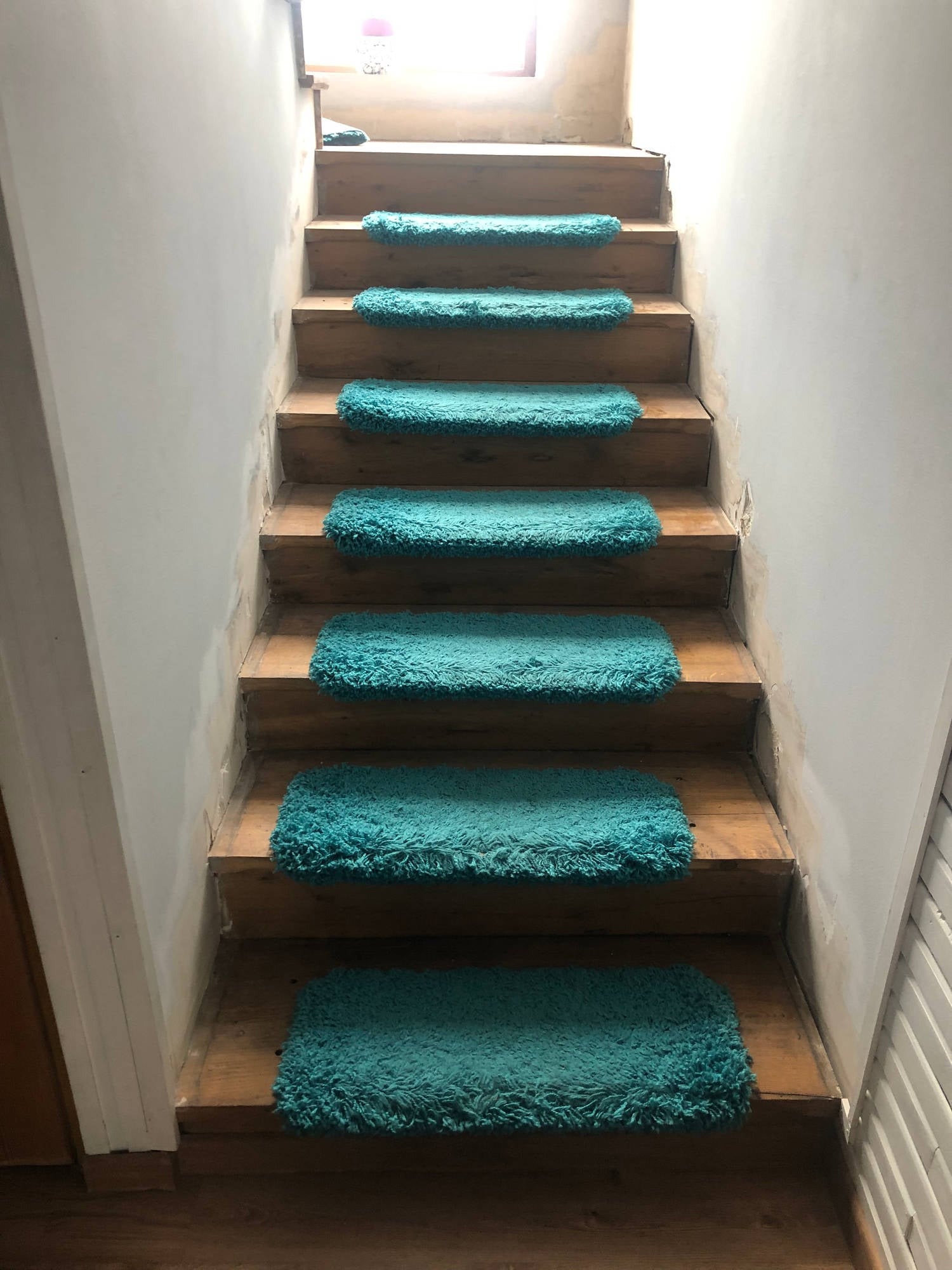 Drewniane schody z turkusowymi dywanikami na stopniach, ściany w trakcie malowania, widoczne ślady po szpachlowaniu.