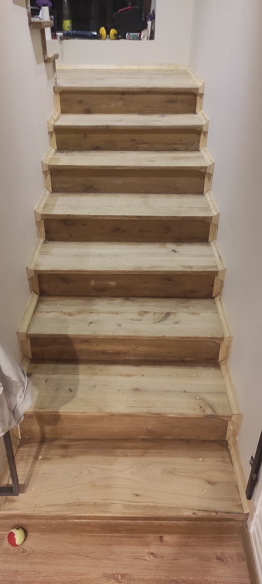 Drewniane schody z jasnego drewna, widok z dołu, z widoczną piłką dla psa na podłodze, świeżo po cyklinowaniu, z widocznymi śladami po szpachli.