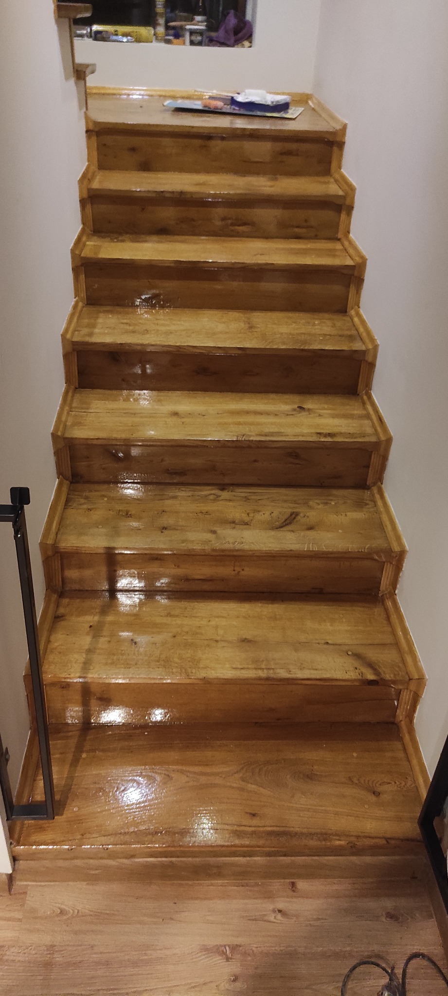 Odnowione drewniane schody z widocznym połyskiem świeżo nałożonego lakieru, jasne drewno stopni i podłogi, białe ściany, ujęcie z góry.