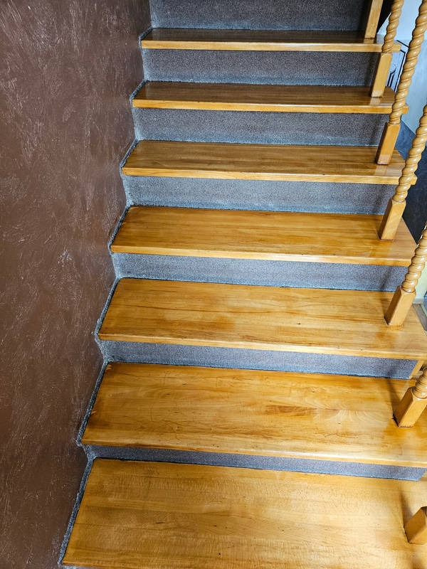 Schody drewniane po cyklinowaniu, z szarym dywanem na podstopnicach, widok z góry na kręcone poręcze.
