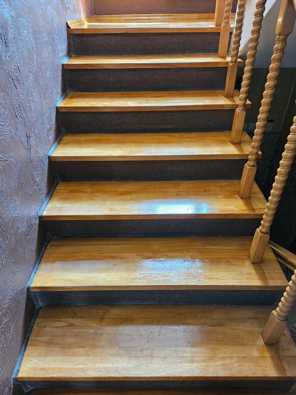 Drewniane schody z kręconą balustradą, widok od dołu, z ciemnymi podstopnicami i połyskującymi stopniami po cyklinowaniu.