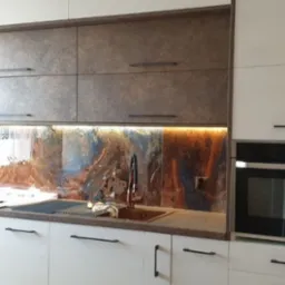 Nowoczesna kuchnia z białymi dolnymi szafkami i g&oacute;rnymi szafkami w kolorze brązu z metalicznym połyskiem, podświetlany panel nad blatem z abstrakcyjnym wzorem w odcieniach brązu i niebieskiego...