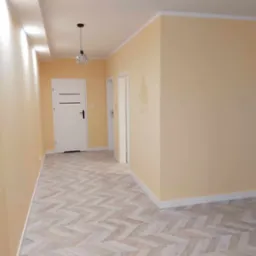 Świeżo pomalowane, jasnożółte ściany w korytarzu w Szydłowie, z nową podłogą w jodełkę i białymi listwami przypodłogowymi oraz ozdobnym żyrandolem.